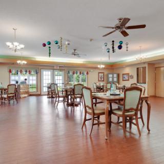 A spacious dining area with wooden floors, elegantly arranged tables and chairs, ceiling fans, and decorative lighting.