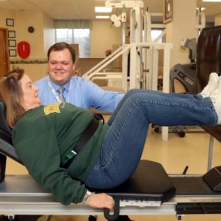 A person receiving physical therapy guidance while exercising with leg press equipment.