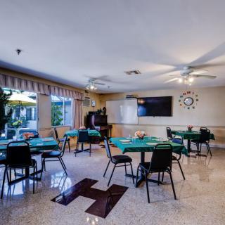 A bright dining area with several tables and chairs, lit by natural light through large windows.