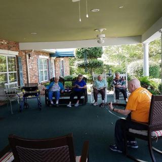 A group of elderly people sitting and conversing on an outdoor porch.