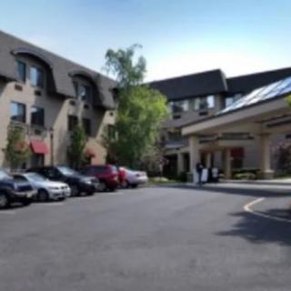 A parking lot in front of a multi-story building with several cars parked and trees nearby.