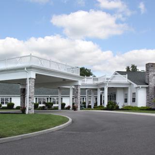 A modern architectural structure with a spacious entrance and landscaped surroundings under a cloudy sky.