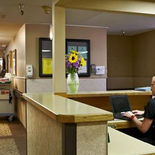 A reception area with a desk, computer, and vase of flowers in a hallway setting.