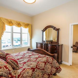 A cozy bedroom featuring a richly patterned bedspread, a wooden dresser with an ornate mirror, and a sunlit window with golden curtains.