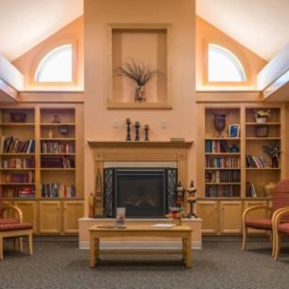 A cozy library room with a central fireplace, surrounded by bookshelves and comfortable seating.