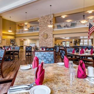 A spacious dining hall with neatly set tables, featuring red napkins and an elegant interior design.