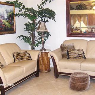 A cozy living room setup featuring two cream-colored sofas, decorative pillows, a potted plant, a lamp on a side table, and framed artwork on the walls.