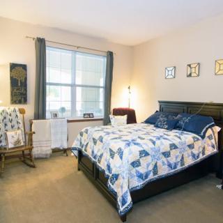 A cozy bedroom with a quilted bedspread, rocking chair, and large window.