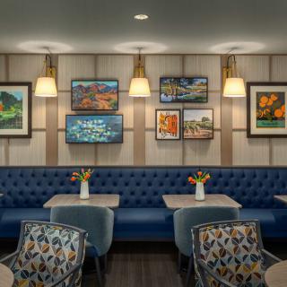 A cozy restaurant interior featuring blue tufted seating, decorated walls with vibrant artwork, and tables adorned with floral arrangements.