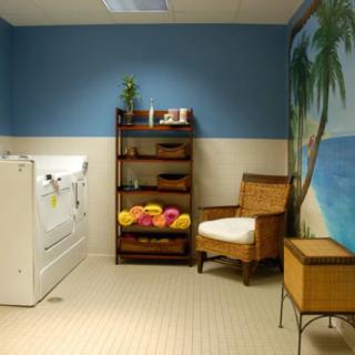 A relaxing tropical-themed bathroom with a bathtub, wicker chair, and shelves stocked with colorful towels.
