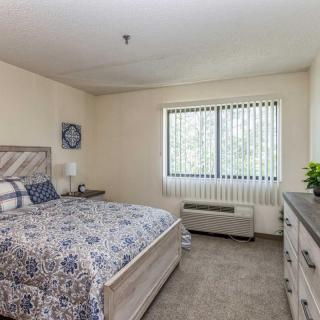 A cozy bedroom with a bed, dresser, and window with vertical blinds.