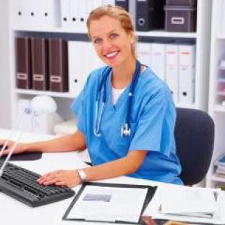 A nurse working at a desk with a computer and stethoscope.