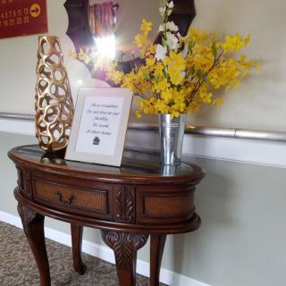 A classic wooden table adorned with a decorative vase and vibrant yellow flowers, accompanied by a framed sign.