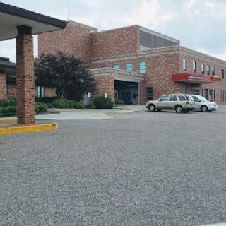 A brick hospital building with a parking lot, under a cloudy sky.