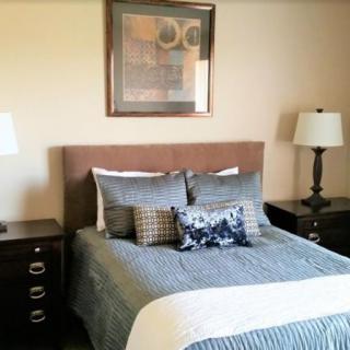 A cozy bedroom with a neatly made bed, flanked by matching nightstands and lamps, and adorned with wall art.