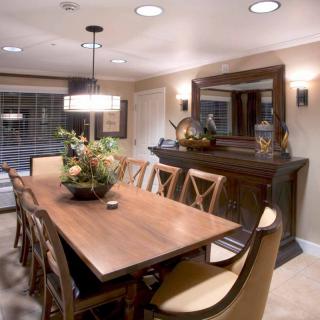 A cozy dining room with a large wooden table, surrounded by chairs and illuminated by elegant lighting.