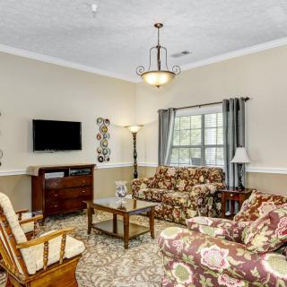 A cozy living room with floral patterned furniture, a television mounted on the wall, and natural light streaming through the windows.
