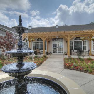 A beautiful courtyard featuring a central fountain, surrounded by well-maintained gardens and a covered patio area.