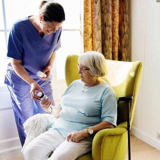 A nurse assists an elderly woman seated in a comfortable chair.
