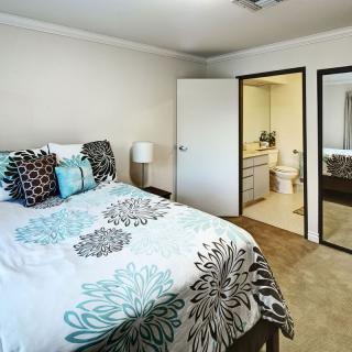 A cozy bedroom with a modern decor, featuring a bed with patterned bedding, a lamp, and an adjoining bathroom visible through an open door.