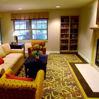 A cozy living room featuring a sofa, armchair, bookshelf, fireplace, and a decorative rug.