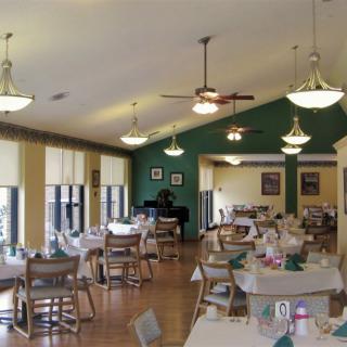 A well-lit dining area with neatly arranged tables and chairs, featuring decorative lighting and large windows.