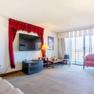 A cozy living room with a large TV, red curtains, and a balcony view.