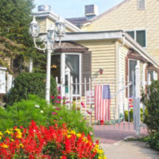 A cozy house with a garden full of vibrant flowers and an American flag by the entrance.
