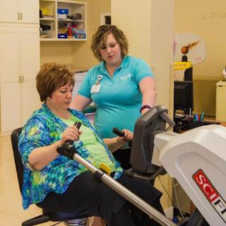 A healthcare professional assists a patient with an exercise machine during a rehabilitation session.