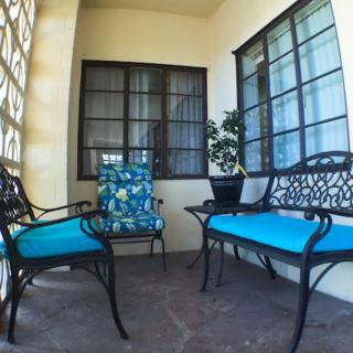 A cozy patio with chairs and a bench featuring bright blue cushions, complemented by a potted plant and large windows.