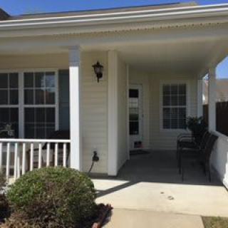 A sunny front porch of a residential house, featuring large windows and a welcoming entrance.