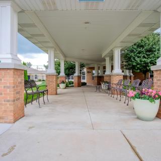 A covered walkway with benches and flower pots leading to a building entrance.