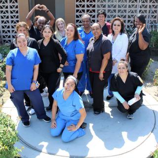 A group of people in medical uniforms posing together outdoors, smiling and making hand gestures.