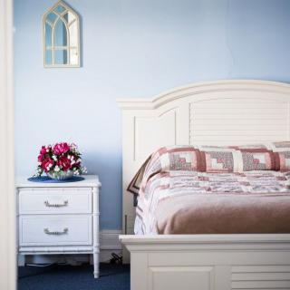 A cozy bedroom featuring a white bed and nightstand with a bouquet of flowers.