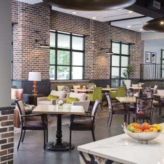A modern restaurant interior with brick walls, featuring neatly arranged tables and chairs in a well-lit dining area.