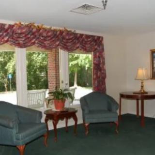 A cozy living room with two chairs, a small table, and a lamp near large windows with decorative curtains.