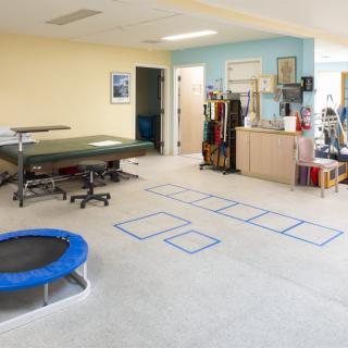 A physical therapy room equipped with various exercise equipment, including a trampoline and mats.