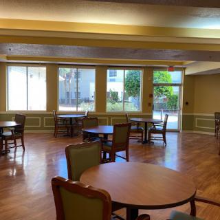 An empty dining area with several tables and chairs, well-lit by large windows.