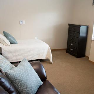 A minimalist bedroom with a single bed, a dark dresser, and a comfortable sofa.