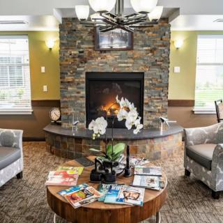 A cozy living room with a stone fireplace, comfortable seating, and magazines on a wooden coffee table.