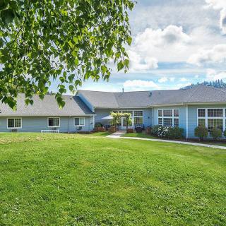 A spacious house with a large green lawn and trees under a partly cloudy sky.