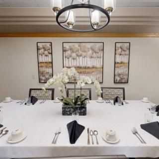 An elegantly set dining table with a white tablecloth, black napkins, and a centerpiece of orchids, beneath a modern chandelier and surrounded by artistic wall decor.