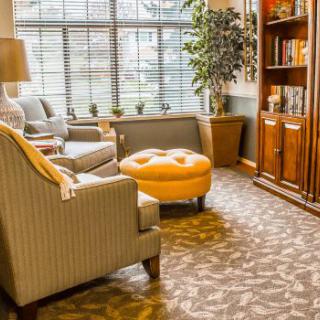 A cozy living room with armchairs, a bookshelf, and a window offering natural light.