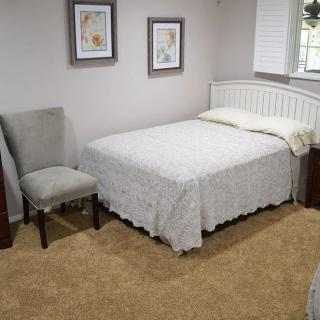 A cozy bedroom with a neatly made bed, a chair, and framed artwork on the walls.
