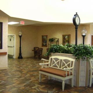 A warmly lit hallway with benches, decorative plants, and a clock.