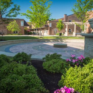 A serene university campus courtyard with manicured gardens and traditional architecture under a clear blue sky.