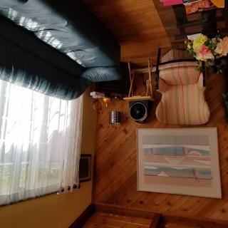 A cozy living room with a couch, chair, and table, featuring artwork on the wall and a view through the curtains.