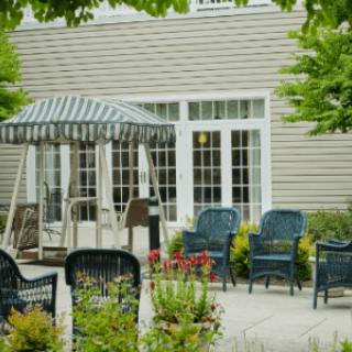 A cozy outdoor patio area featuring a swing, multiple chairs, and lush greenery.