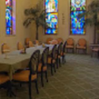 A dining room with stained glass windows and arranged chairs around tables.