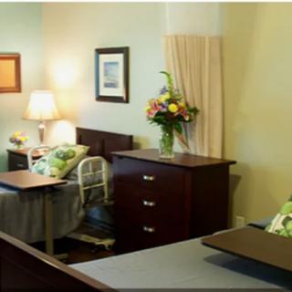 A hospital room with two beds, a lamp, and a bouquet of flowers on a dresser.